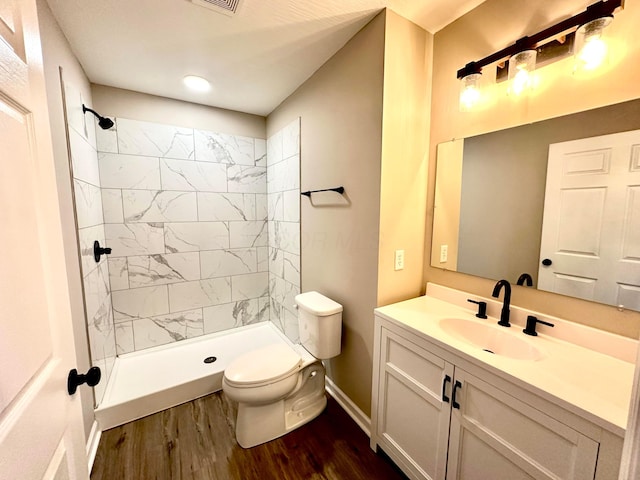 bathroom featuring hardwood / wood-style floors, vanity, toilet, and a tile shower