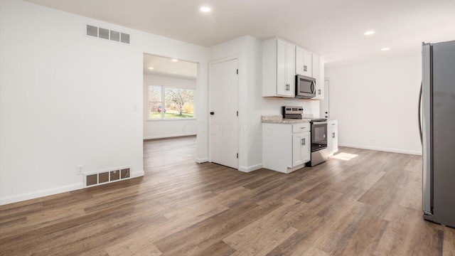 kitchen with white cabinetry, hardwood / wood-style floors, light stone counters, and appliances with stainless steel finishes