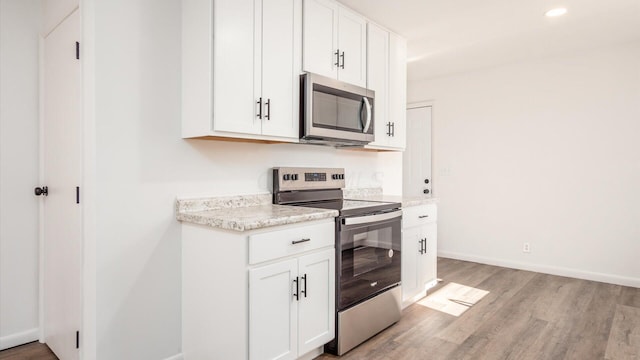 kitchen with light stone counters, light hardwood / wood-style flooring, white cabinets, and appliances with stainless steel finishes