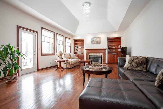 living room with hardwood / wood-style floors, vaulted ceiling, built in shelves, a fireplace, and a chandelier