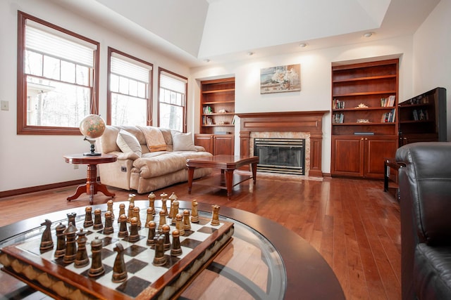 living room featuring a high end fireplace, hardwood / wood-style floors, built in features, and lofted ceiling