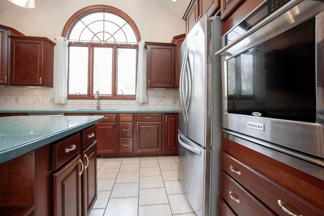 kitchen featuring lofted ceiling, sink, decorative backsplash, light tile patterned flooring, and stainless steel appliances