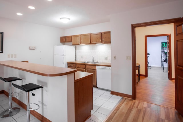 kitchen with white appliances, sink, light hardwood / wood-style flooring, a kitchen bar, and kitchen peninsula