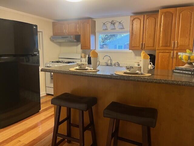 kitchen featuring a breakfast bar, black fridge, light hardwood / wood-style flooring, white gas stove, and extractor fan