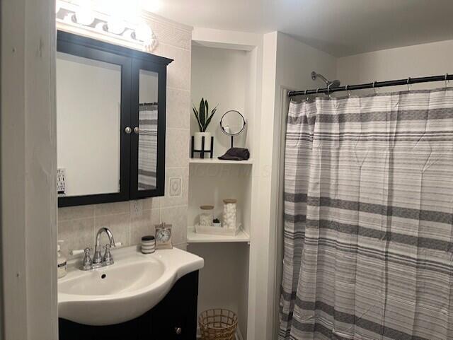 bathroom with vanity, curtained shower, backsplash, and tile walls