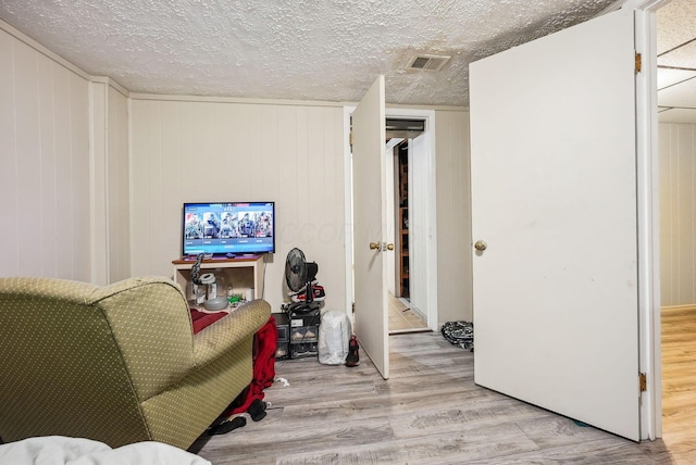 living area with wooden walls, light hardwood / wood-style floors, and a textured ceiling