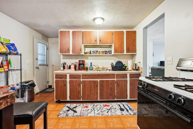 kitchen featuring white gas stove, light parquet flooring, a textured ceiling, and sink