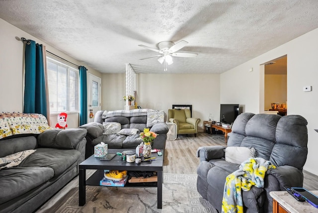 living room with ceiling fan, a textured ceiling, and light hardwood / wood-style flooring