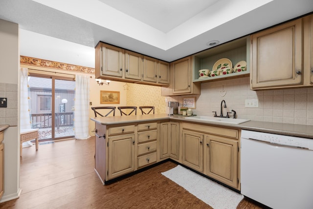 kitchen featuring dishwasher, sink, hardwood / wood-style flooring, decorative backsplash, and kitchen peninsula