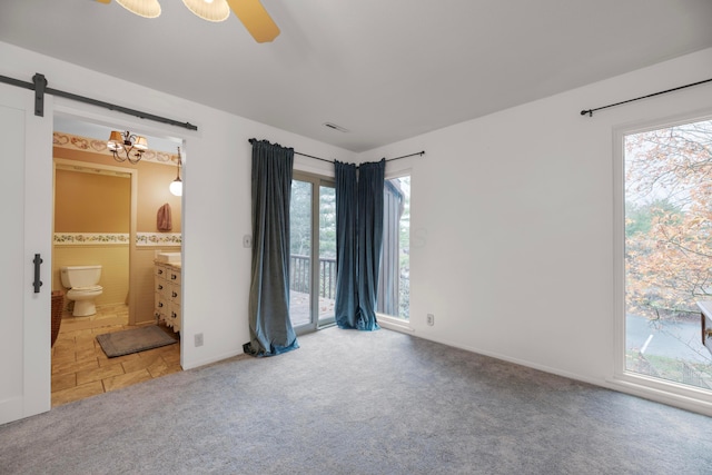 unfurnished bedroom featuring access to outside, ensuite bath, carpet flooring, ceiling fan, and a barn door