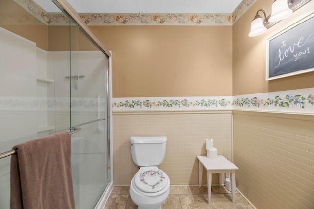 bathroom with toilet, a shower with door, and tile walls