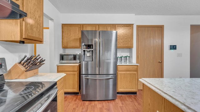 kitchen with a textured ceiling, stainless steel appliances, range hood, and light hardwood / wood-style floors