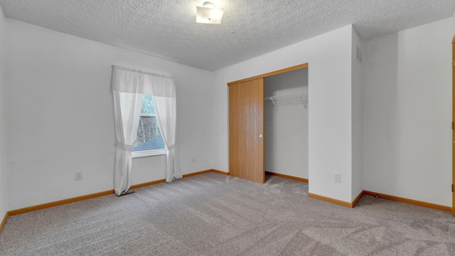 unfurnished bedroom featuring a textured ceiling, light colored carpet, and a closet