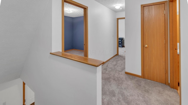 hallway with light colored carpet and a textured ceiling