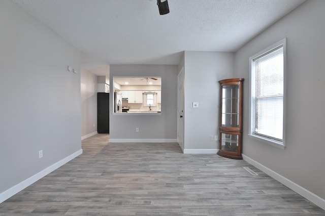 unfurnished living room with a textured ceiling, light hardwood / wood-style floors, and ceiling fan