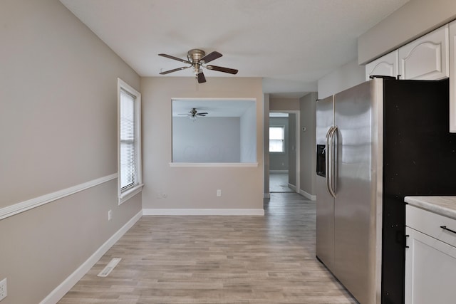 kitchen with stainless steel fridge, light wood-type flooring, white cabinetry, and plenty of natural light