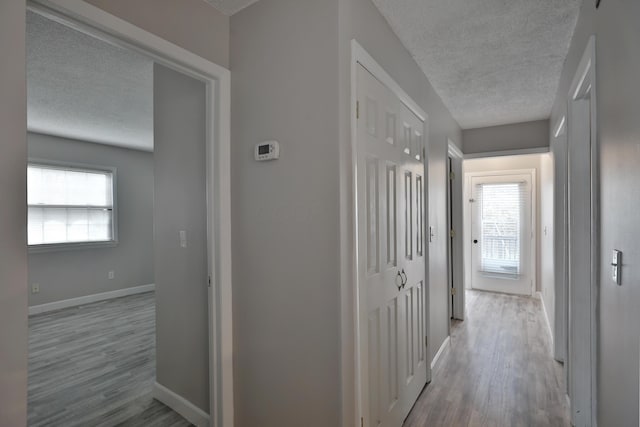 corridor with a textured ceiling and light hardwood / wood-style floors