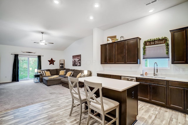 kitchen featuring a kitchen breakfast bar, vaulted ceiling, sink, light hardwood / wood-style floors, and a kitchen island