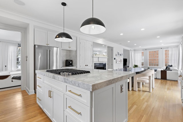 kitchen with white cabinetry, light stone counters, a center island, pendant lighting, and stainless steel appliances