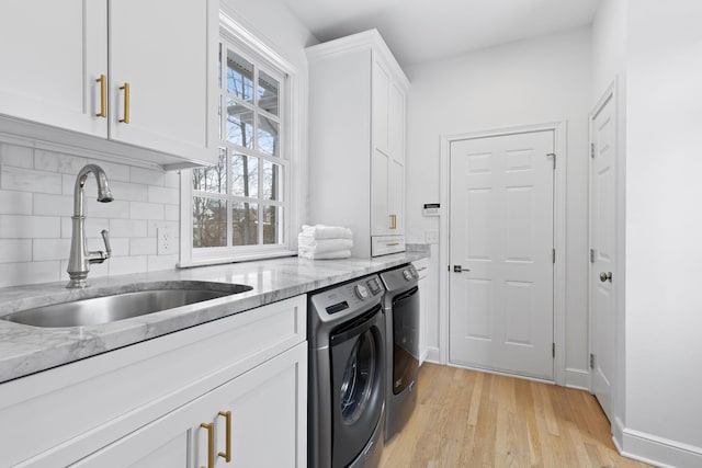 clothes washing area featuring sink, light hardwood / wood-style flooring, washing machine and dryer, and cabinets