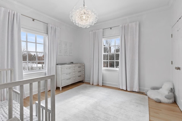 bedroom featuring a notable chandelier, crown molding, light hardwood / wood-style floors, and a nursery area