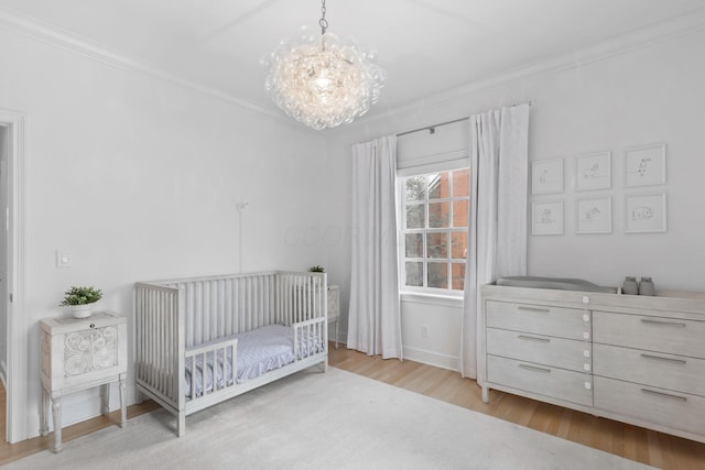 bedroom featuring a nursery area, crown molding, light hardwood / wood-style flooring, and a notable chandelier