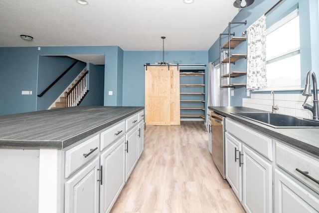 kitchen with white cabinetry, sink, a barn door, stainless steel dishwasher, and light hardwood / wood-style floors