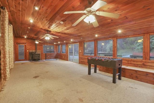 game room featuring a wood stove, wood walls, light colored carpet, and wood ceiling