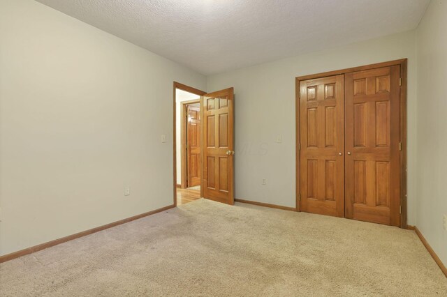 unfurnished bedroom featuring a textured ceiling, light colored carpet, and a closet