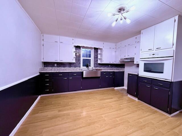 kitchen with white cabinets, light hardwood / wood-style flooring, sink, and white oven