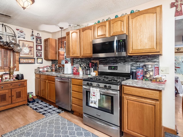 kitchen featuring sink, a textured ceiling, appliances with stainless steel finishes, and light hardwood / wood-style flooring