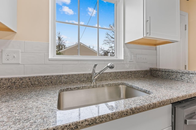 kitchen with light stone counters, white cabinetry, sink, and tasteful backsplash