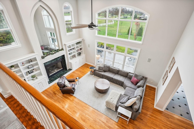 living room featuring ceiling fan, wood-type flooring, a fireplace, and a high ceiling