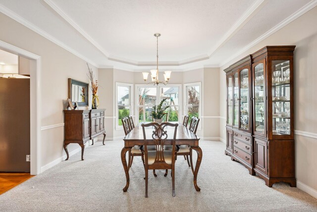 carpeted dining area featuring a raised ceiling, crown molding, and an inviting chandelier