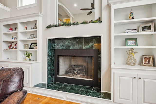 details featuring a tile fireplace, hardwood / wood-style flooring, built in features, and ceiling fan