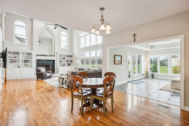 dining room featuring built in features, ceiling fan with notable chandelier, light hardwood / wood-style flooring, and a premium fireplace