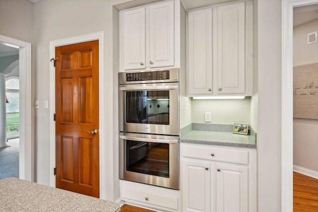 kitchen featuring stainless steel double oven, light hardwood / wood-style floors, and white cabinetry