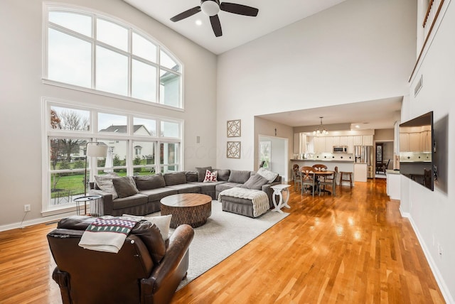 living room featuring ceiling fan with notable chandelier, a towering ceiling, and hardwood / wood-style flooring