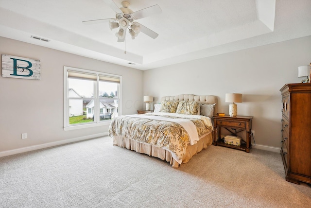 carpeted bedroom with ceiling fan and a raised ceiling