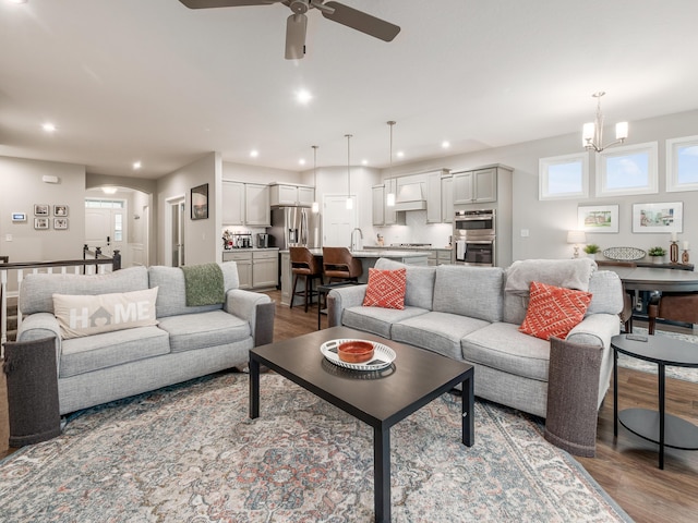 living room featuring wood-type flooring, ceiling fan with notable chandelier, and sink