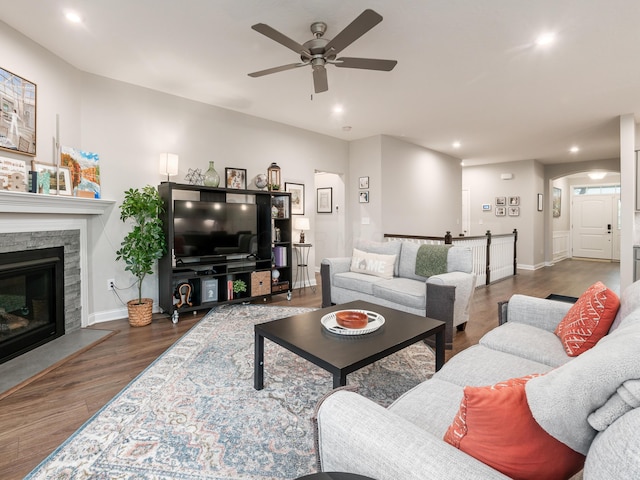 living room with a fireplace, ceiling fan, and dark wood-type flooring