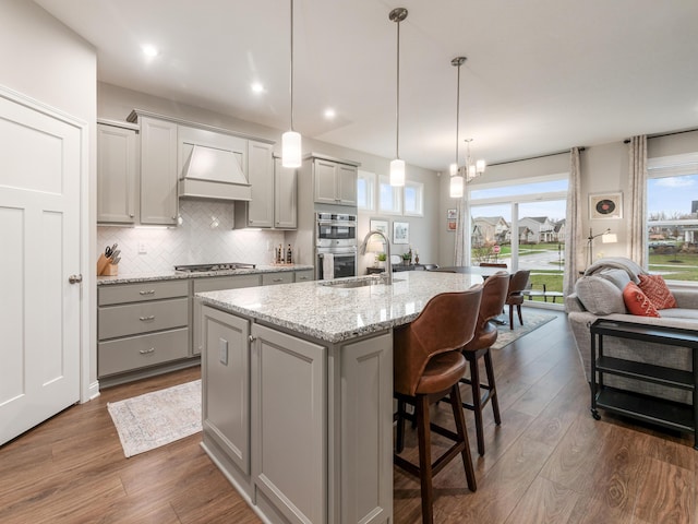 kitchen featuring hanging light fixtures, dark hardwood / wood-style floors, an island with sink, gray cabinets, and custom exhaust hood