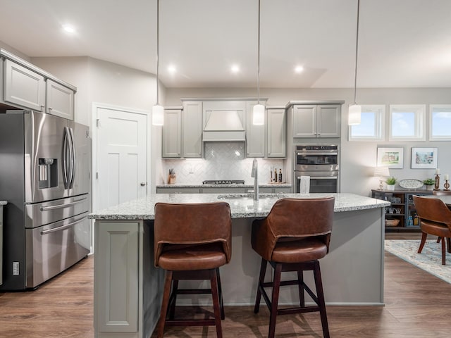 kitchen with a center island with sink, light stone counters, appliances with stainless steel finishes, decorative light fixtures, and dark hardwood / wood-style flooring