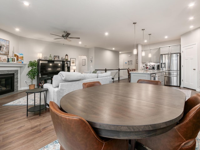 dining area with a fireplace, light wood-type flooring, and ceiling fan