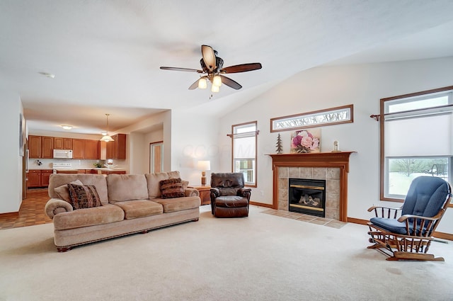 carpeted living room with ceiling fan, lofted ceiling, and a tiled fireplace