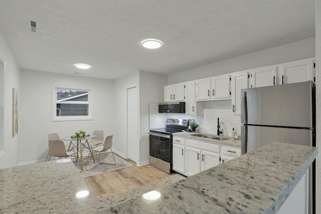 kitchen with appliances with stainless steel finishes, light wood-type flooring, a textured ceiling, sink, and white cabinets