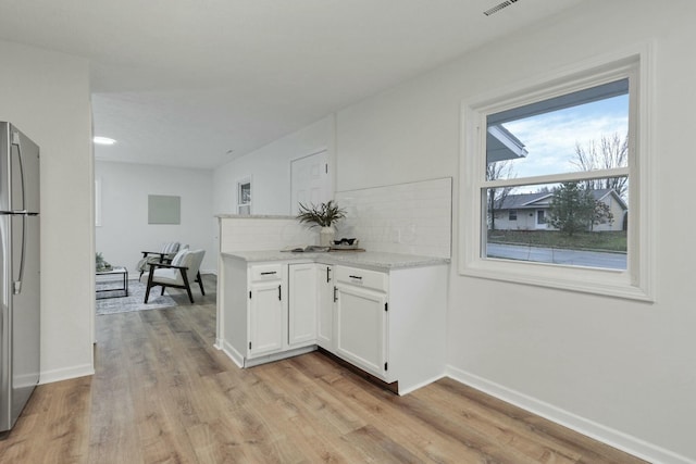 kitchen with tasteful backsplash, light stone counters, white cabinets, light hardwood / wood-style floors, and stainless steel refrigerator