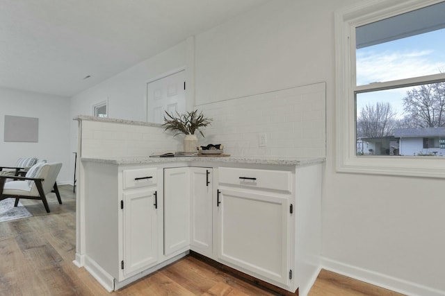 kitchen with backsplash, light stone countertops, light hardwood / wood-style flooring, and white cabinets