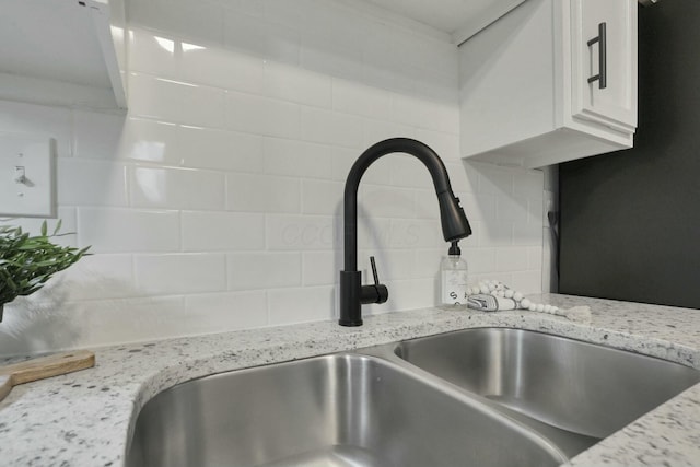 room details featuring backsplash, white cabinetry, light stone countertops, and sink