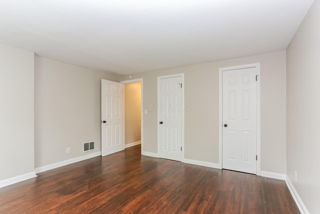 unfurnished bedroom featuring dark hardwood / wood-style flooring and multiple closets